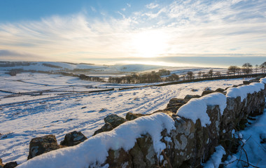 A snowy wall lines the view of a lovely cold sunset in the Peak District