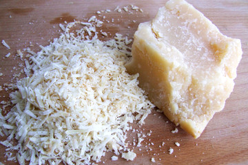 piece of Parmesan cheese on a wooden board and grated cheese. сlose up