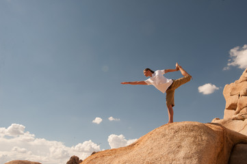 Young man in Dancer's Pose high up on a rock boulder. 