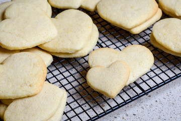 Stacks of heart shaped sugar cookies on a black wire cooling rack, granite kitchen counter