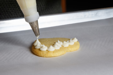 Close up of vanilla frosting being piped onto a heart shaped sugar cookie
