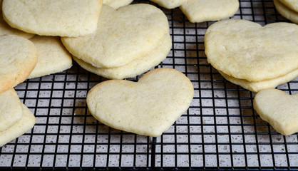 Stacks of heart shaped sugar cookies on a black wire cooling rack, granite kitchen counter