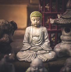 A small little Buddha statue with a green hat hidden away with other figurines in a market