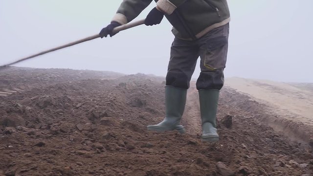 senior farmer with hat holding a muddy hoe and pitchfork on the field. Manual labor. Fog
