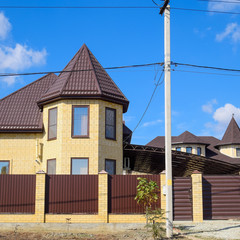 Decorative metal on the roof of a brick house. Fence made of corrugated metal.