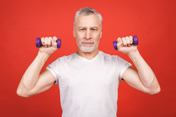 Obraz na płótnie Canvas Portrait Of A Senior Man Exercising with dumbbells against red Background.