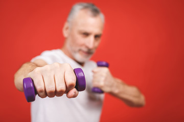 Close-up portrait Of A Senior Man Exercising with dumbbells against red Background.
