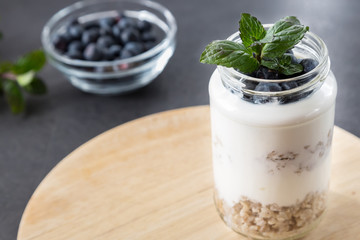 goblet of yogurt with cereals and fruits strewed on leaves mint
