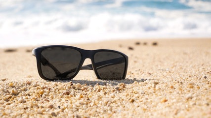 Fototapeta na wymiar Close up of sunglasses on a sandy beach in summer. Shallow focus.
