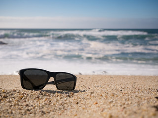 Fototapeta na wymiar Sunglasses lying on sandy beach. shallow depth of field.