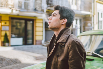 Portrait of a model young handsome sexy male brunette guy with dark skin Turkish Middle Eastern brunette posing smoking a cigarette near old retro car on the street