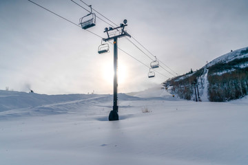 Fototapeta na wymiar Bright sun over ski lifts on snow covered mountain