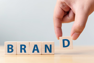 Hand of male putting wood cube block with word “BRAND” on wooden table. Brand building for...