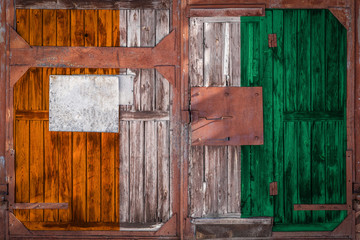 Close-up of old warehouse gate with national flag of  Cote d'Ivoire. The concept of  Cote d'Ivoire export-import, storage of goods and national delivery of goods. Flag in grunge style