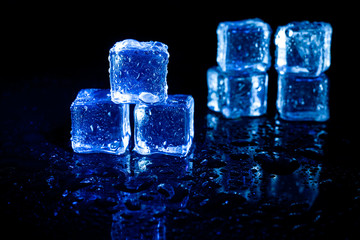Blue ice cubes reflection on black table background.