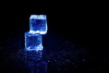 Blue ice cubes reflection on black table background.