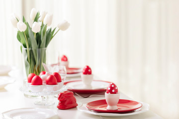 Happy easter. Decor and table setting of the Easter table is a vase with white tulips and dishes of red and white color. Easter colored eggs with white polka dots.