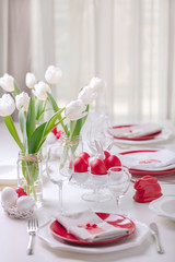 Happy easter. Decor and table setting of the Easter table is a vase with white tulips and dishes of red and white color. Easter colored eggs with white polka dots.