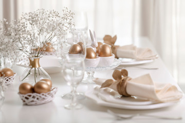 Happy Easter! Golden decor and table setting of the Easter table with white dishes of white color.