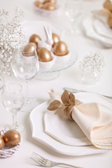 Happy Easter! Golden decor and table setting of the Easter table with white dishes of white color.