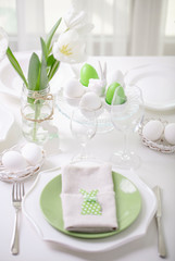 Decor and table setting of the Easter table with white tulips and dishes of green and white color. Easter decor in the form of Easter bunnies  green color with white polka dots.