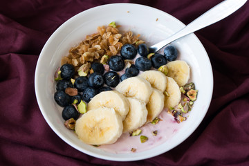Bowl of fresh blueberries, banana and muesli yogurt on red color table clothes