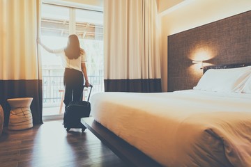 Asian women are staying in a hotel room. Open the curtain in the room Along with carrying luggage.Concept of people be comfortable to travel. - obrazy, fototapety, plakaty