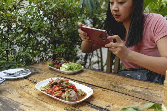 Woman is taking a photo of Thai food on the table.