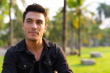 Face of young handsome Hispanic man thinking in the park