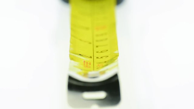 Extreme closeup of a yellow tape measure - with inch and centimeters labeled in black - focus moving from number 1, 2, etc..