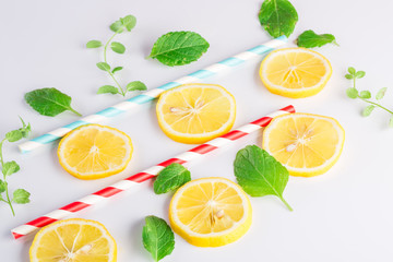 Colorful drinking paper straws and mint leaves, lemon slices on a white background