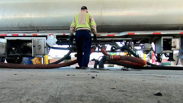 High definition low angle footage of a driver unloading fuel using hoses from a tractor trailer fuel tanker.