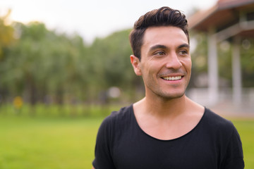 Face of happy young handsome Hispanic man thinking at the park