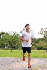 Full body shot of young handsome Hispanic man jogging at the park