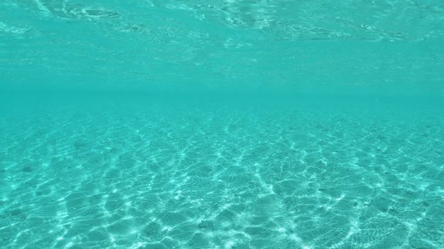 SLOW MOTION, UNDERWATER: Stunning slow motion shot of the tranquil ocean water and the endless sandy ocean floor. Beautiful serene seascape of the turquoise colored Pacific ocean on a sunny summer day