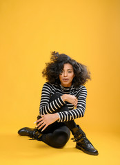 Young Black Woman in a Stripped Shirt sitting on a yellow background