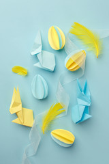 Easter holiday creative background with papercraft eggs, origami bunny on pastel blue table, trendy paper craft holiday background, top view, copy space