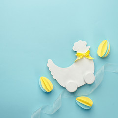 Easter holiday creative background with papercraft eggs, white wooden chicken hun on pastel blue table, trendy paper craft holiday background, top view, copy space