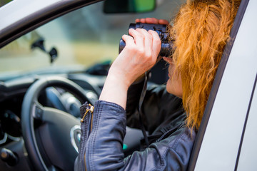 a woman sits in a car and watches with binoculars