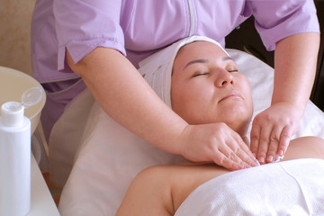 A girl of Asian appearance in a beauty salon. A professional beautician rubs the neck and chest of a Muslim woman with a cleansing lotion. The procedure for rejuvenating women's skin.