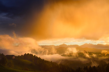 Golden clouds and fog at sunrise in the mountains of Kamnik Savinja Alps in Skofjelosko Hills with St Thomas church near Ljubljana Slovenia