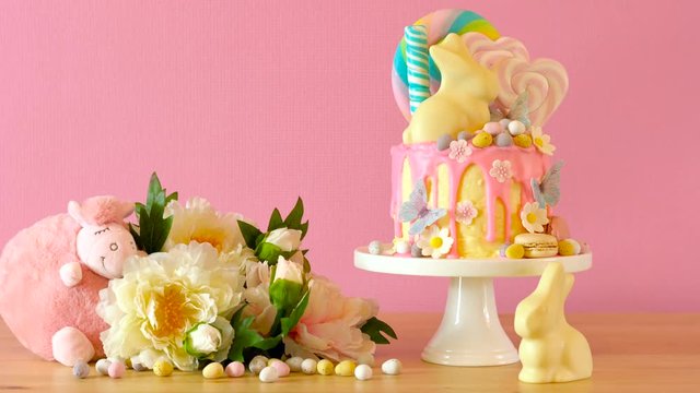 On-trend Easter theme candy land drip cake decorated with lollipops, cand eggs and white chocolate bunny in party table setting.