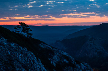 Obraz premium bright red dawn in the mountains in a windy, cloudy morning, the sun rises from the horizon