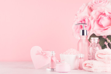 Cosmetics products for bath, spa - essential oil, bath salt, cream, liquid soap, towel, heart and pink roses  in delicate pastel pink  bathroom interior.