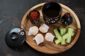 Round wooden serving tray with chinese prawn hargows, elevated view on a dark brown stone background