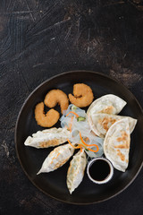 Metal tray with various fried potstickers and panko breaded shrimps, flatlay on a dark brown stone background with space