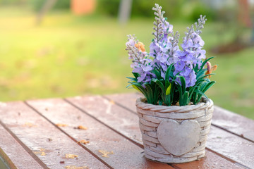 Artificial lavender flowers in metal vase on wood table.
