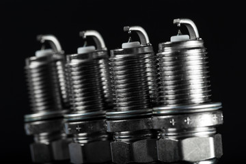 A set of new spark plugs of the car, and spare parts of vehicles on a dark background.