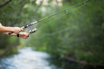 Fishing rod and reel in hands on the river