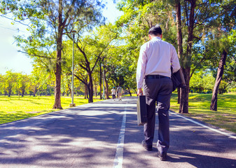 Businessman walking on road in park. He is drinking coffee and holding business bag. Photo concept business bag and relax time.